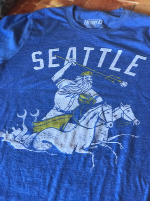 Blue unisex crew t-shirt by Factory 43. It says Seattle and has a mariner wearing a baseball hat and glove and being pulled by two horse mermaids. 