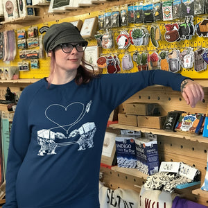 Person wearing a blue sweatshirt with Love AT-AT First Sight design in a store with various items on shelves.