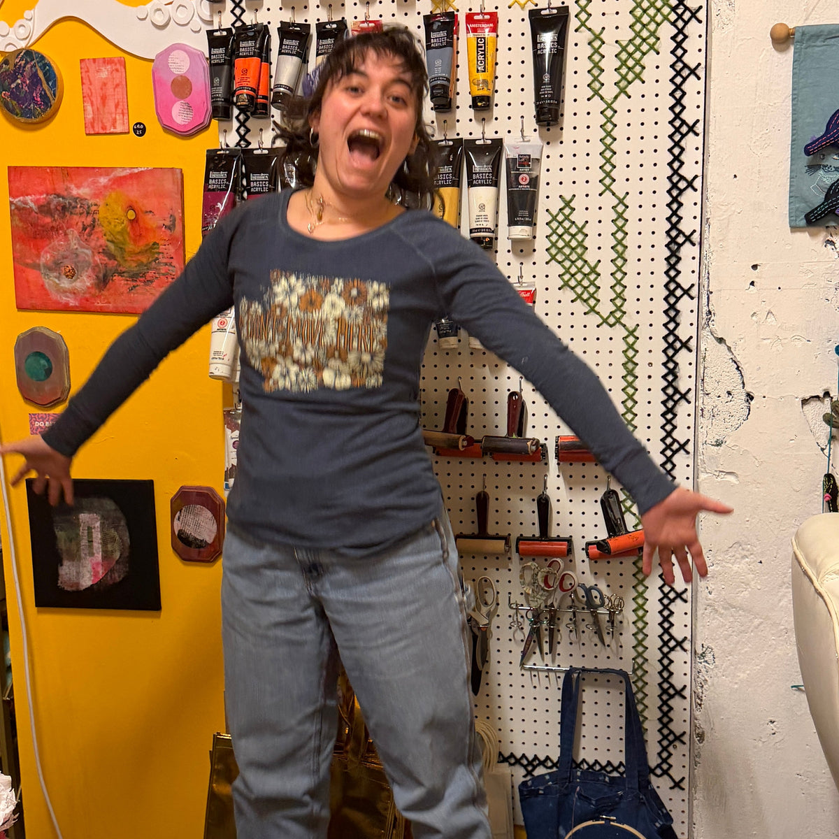 Person in a gray shirt and pants standing in a room with artistic decorations and tools.