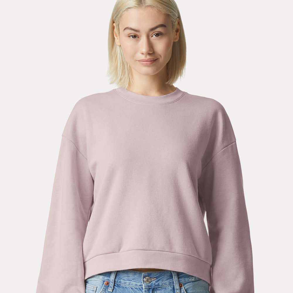 Person wearing a blush pink  sweatshirt and blue jeans on a plain background