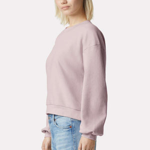 Woman wearing a blush pink sweatshirt and blue jeans on a white background. 