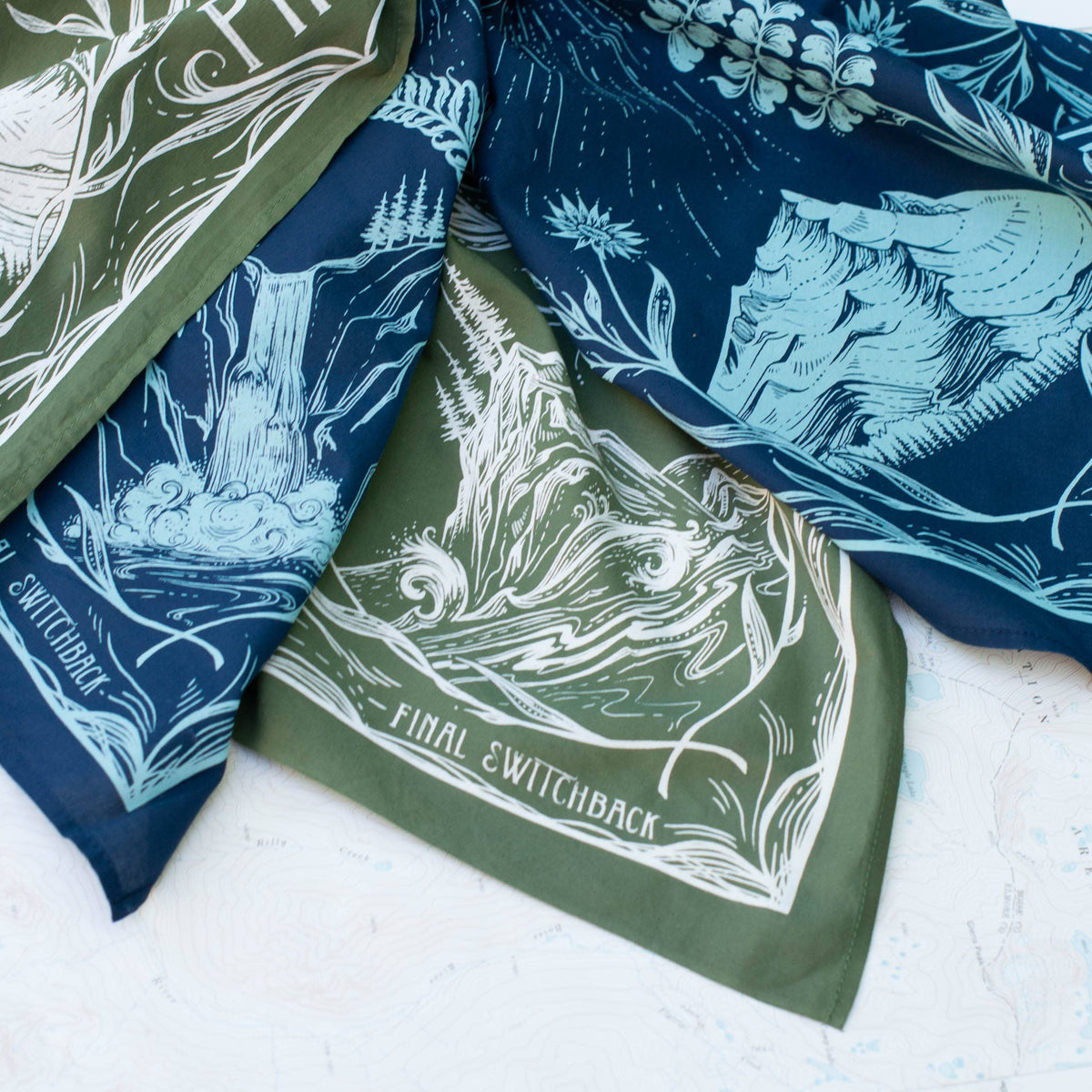 Green and blue bandanas with nature-themed designs on a white surface.