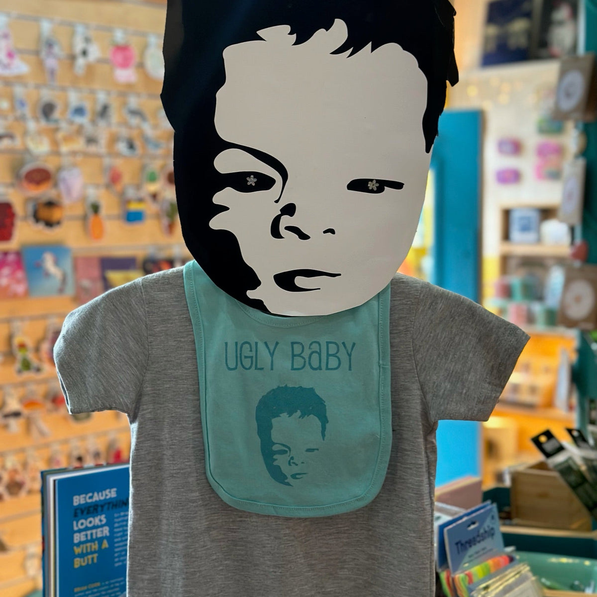 T-shirt with a graphic design of a face and text 'UGLY BABY' in a store setting.