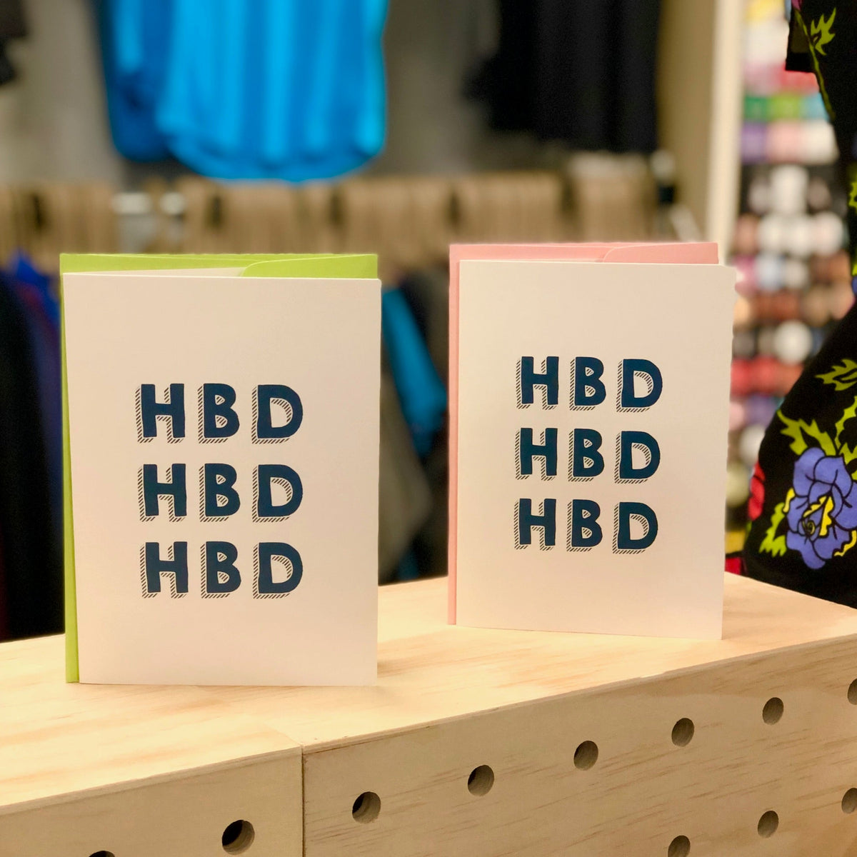 Two greeting cards that say "HBD HBD HBD" sitting atop a wood box. 