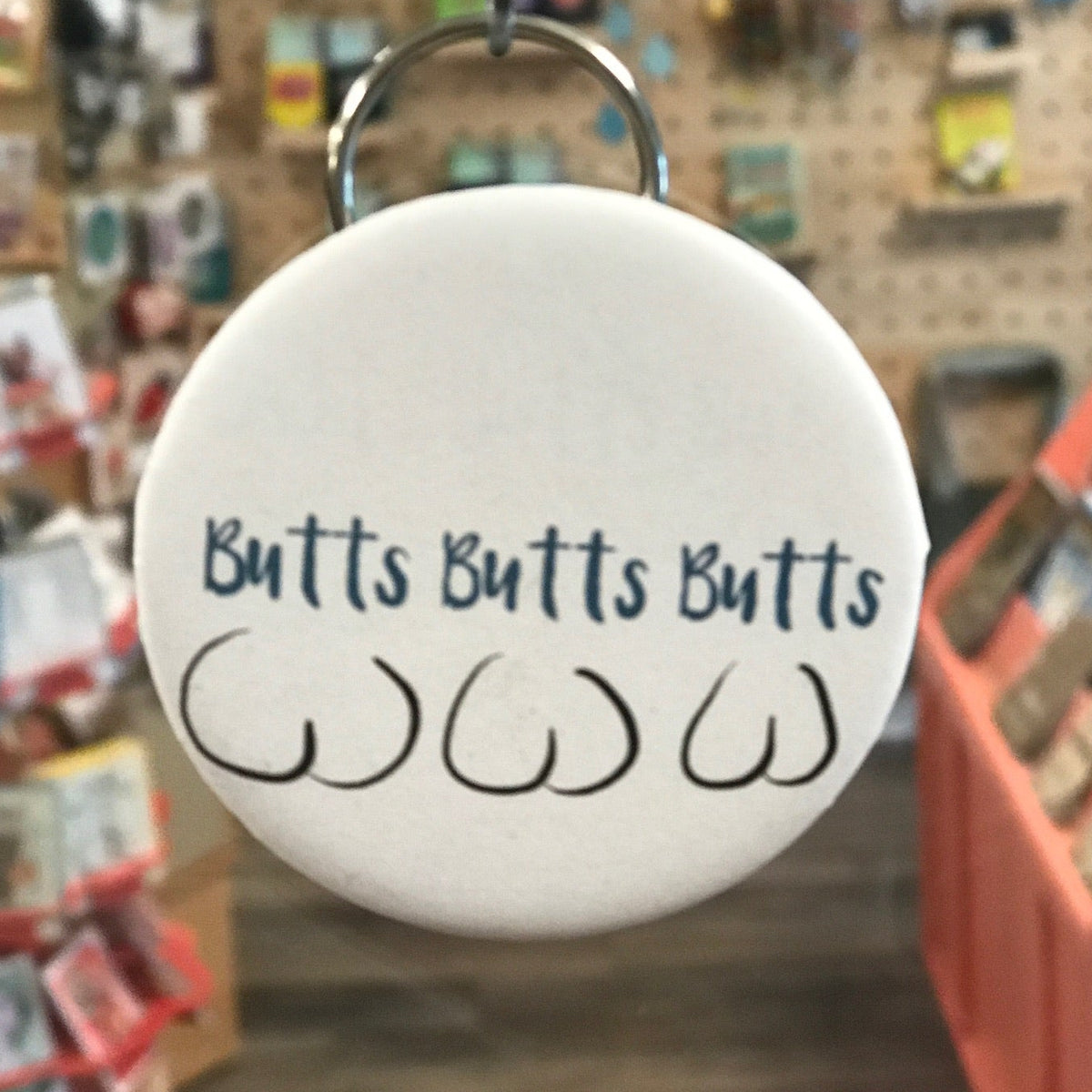 Bottle opener keychain with 'Butts Butts Butts' text in a store setting. 