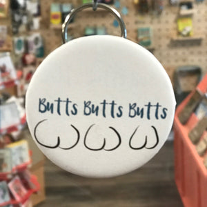 Bottle opener keychain with 'Butts Butts Butts' text in a store setting. 