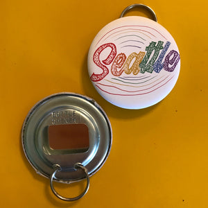 Metal bottle opener with a colorful 'Seattle" made of raindrops on a yellow background. 