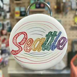 Round keychain with 'Seattle' in colorful letters against a blurred store background