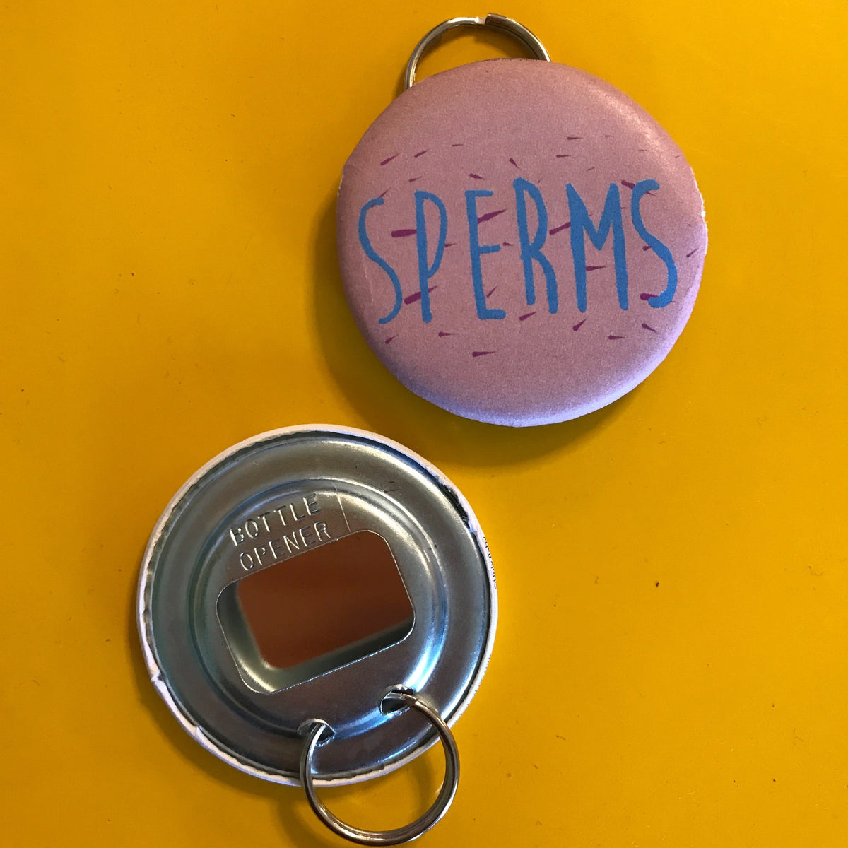 Bottle opener that says 'SPERMS' in blue on a pink background. 