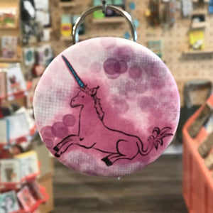 Unicorn keychain with pink and purple design in a store setting. 