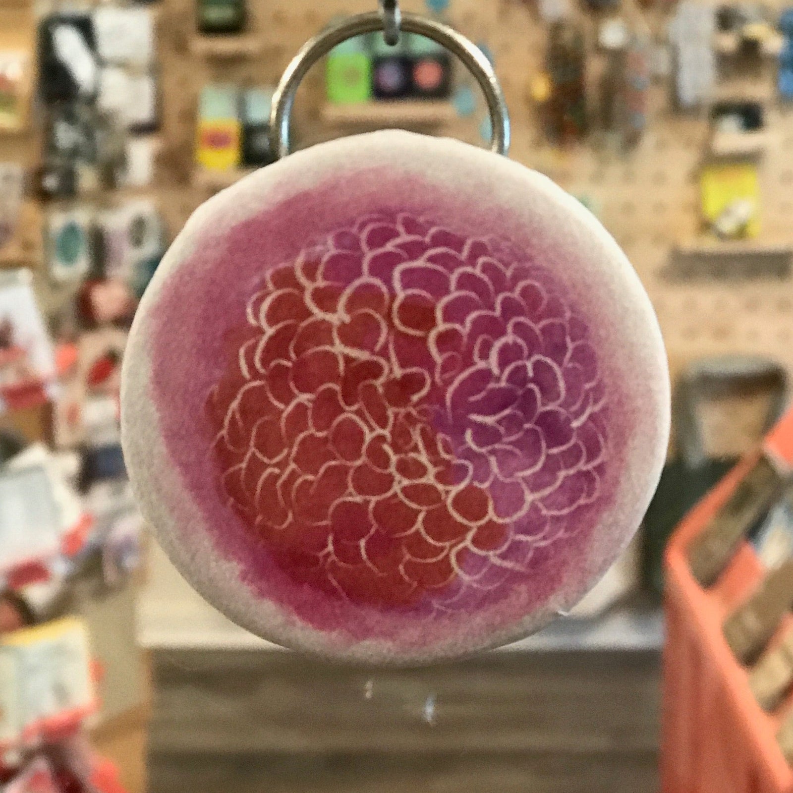 Round pink and purple bottle opener keychain with watercolor floral pattern in a store setting. 