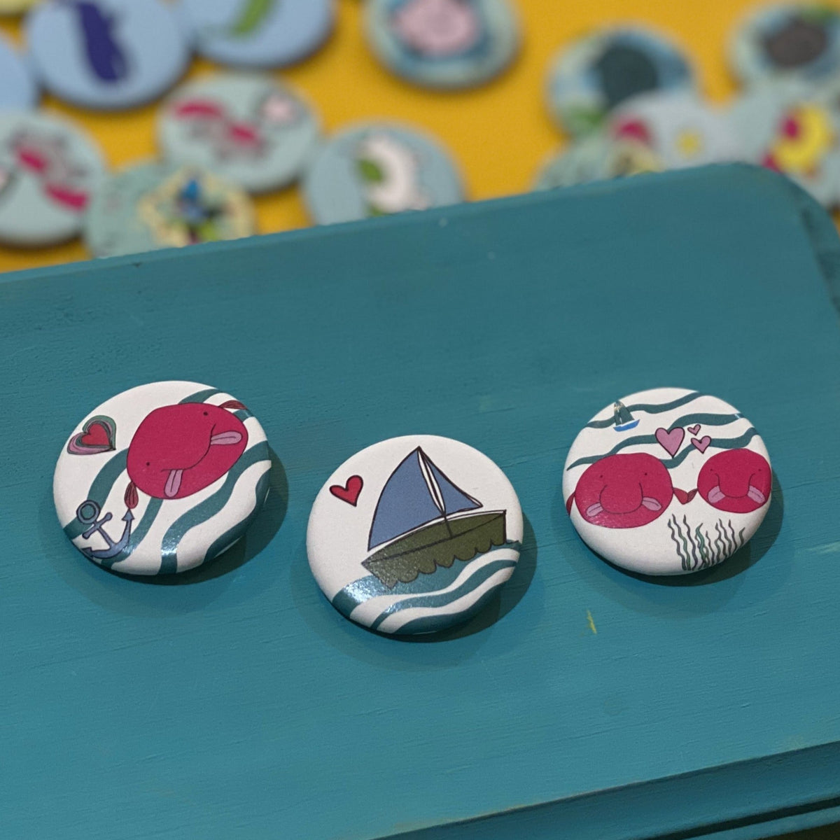 Three colorful Blob Fish themed buttons on a teal surface with more buttons in the background.