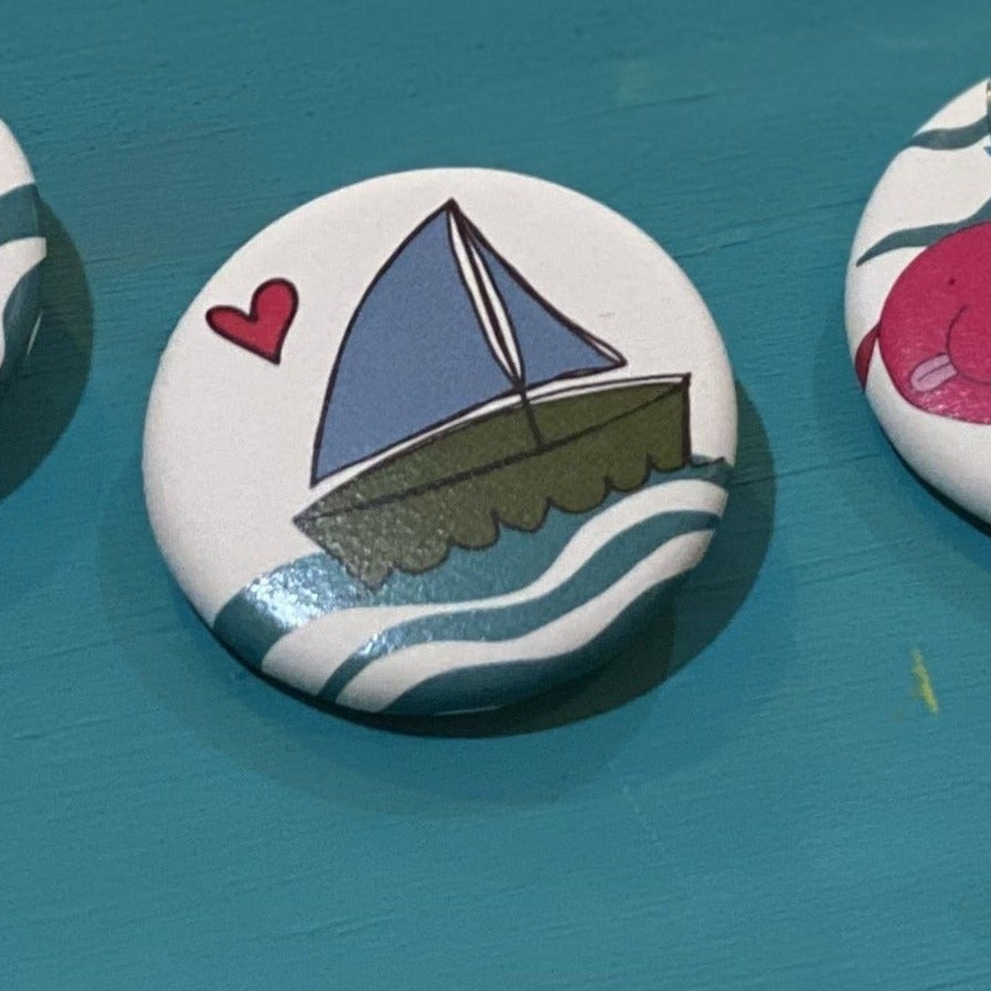 A round button with a sailboat illustration on a blue background. 
