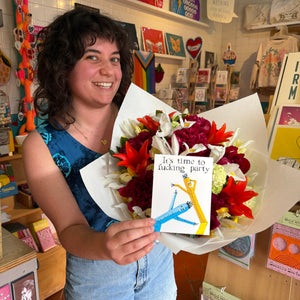Woman holding a bouquet of flowers and a card with a colorful design in a store setting.
