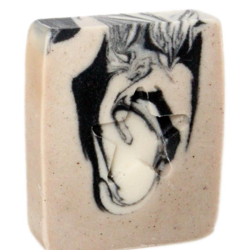 A bar of handmade soap with a swirled pattern design, predominantly in beige color with dark gray and black accents, and speckled with white.
