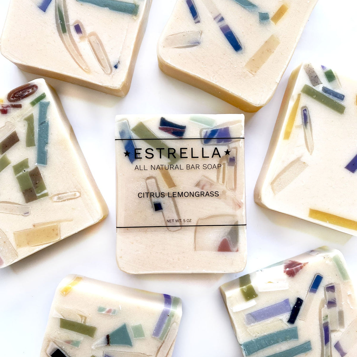 Handmade bar soap with a 'Estrella All Natural Bar Soap' label and 'Citrus Lemongrass' written on it, surrounded by pieces of soap with a mix of multicolored embedded elements.