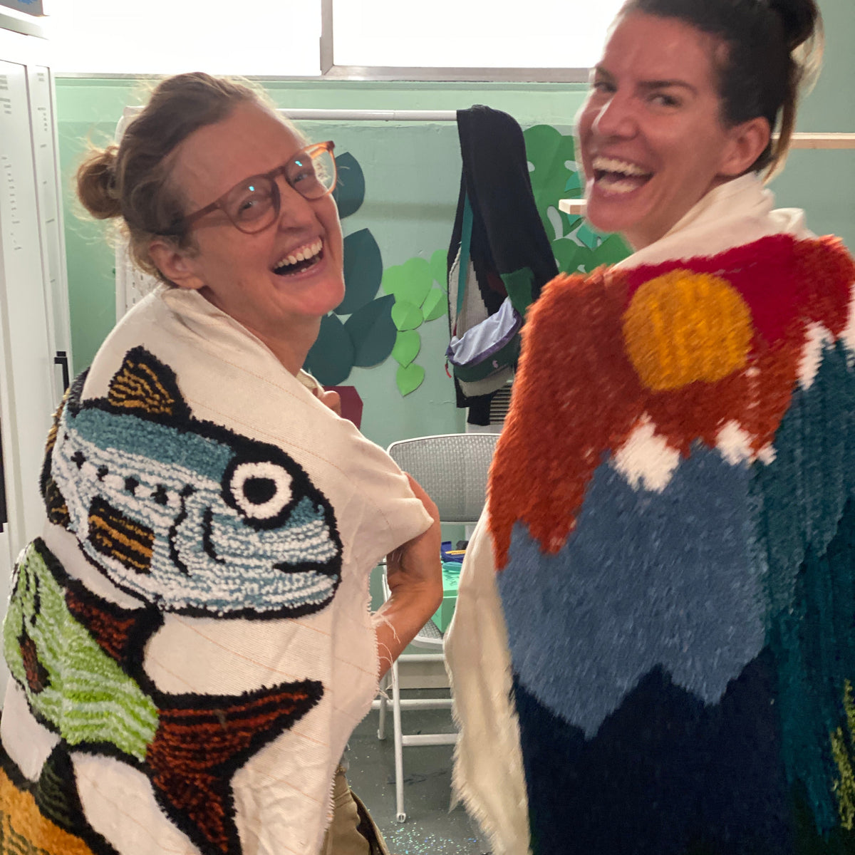 Two people wearing their tufted art pieces as capes.