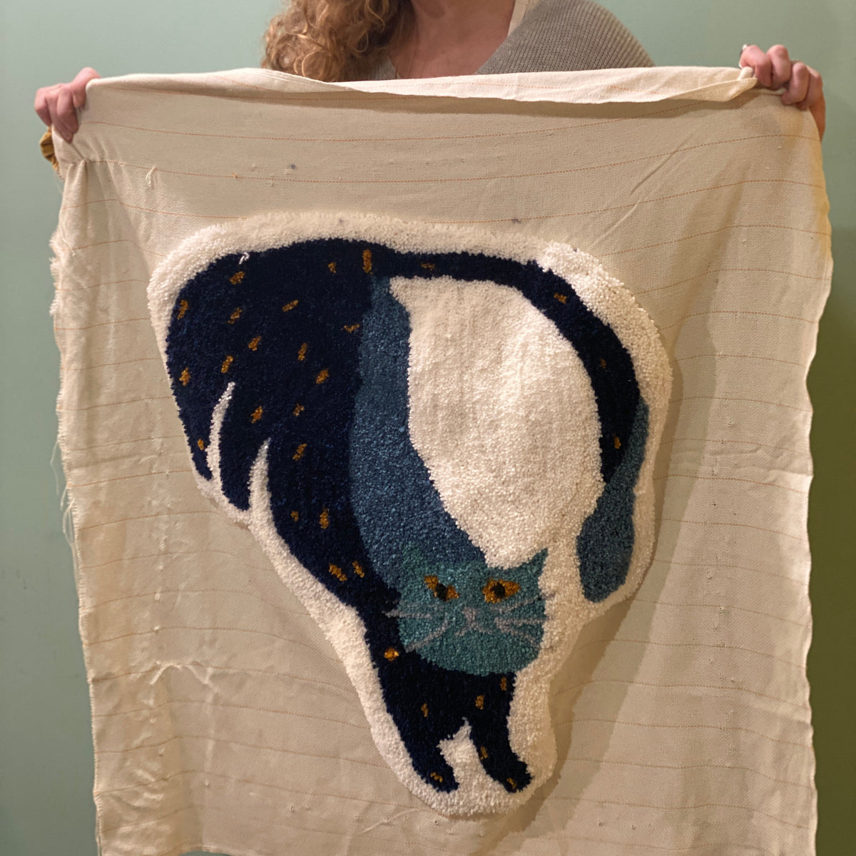 Woman holding a large white fabric with a black cat design tufted on it. 