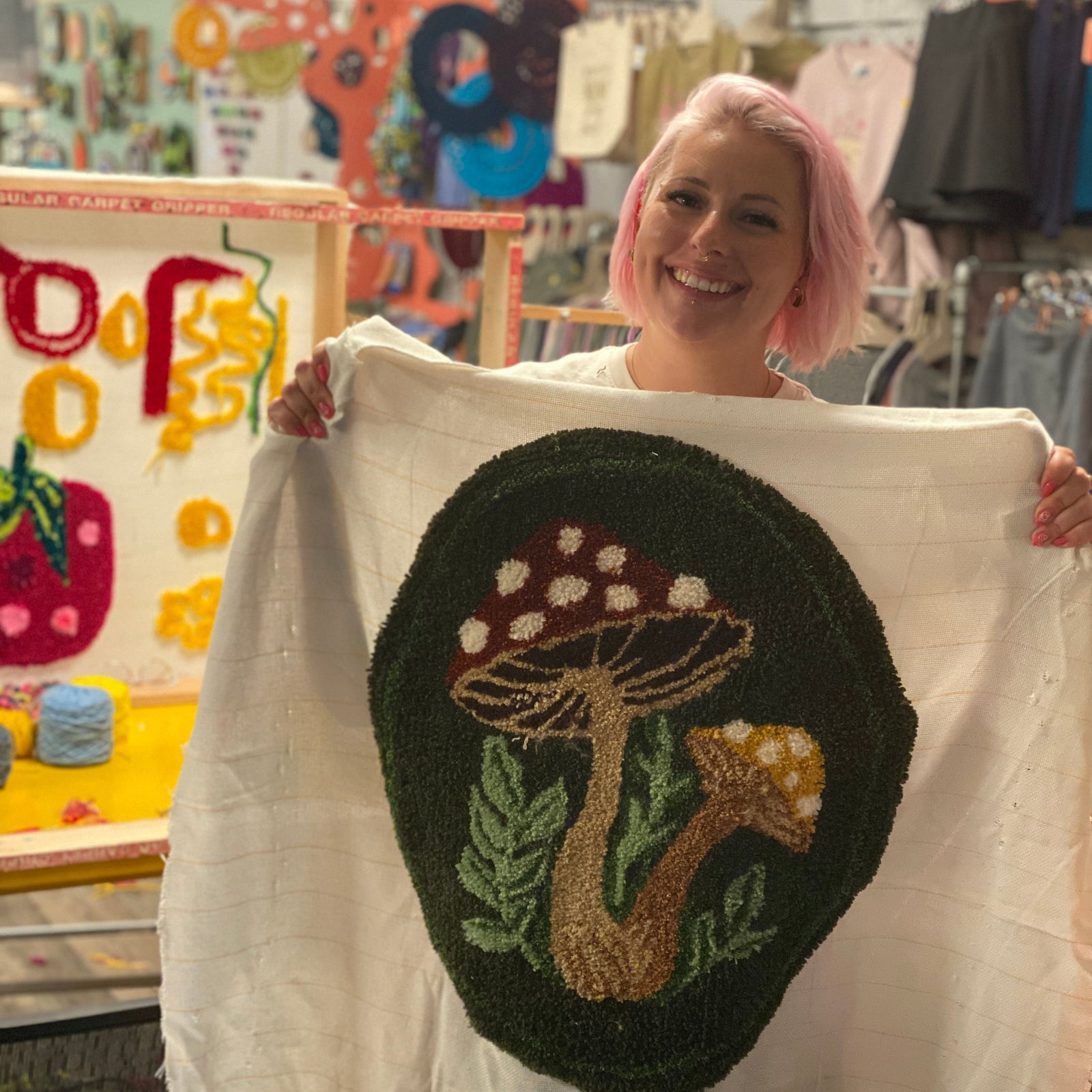 Person holding a tufted mushroom design on a white fabric in a craft store.
