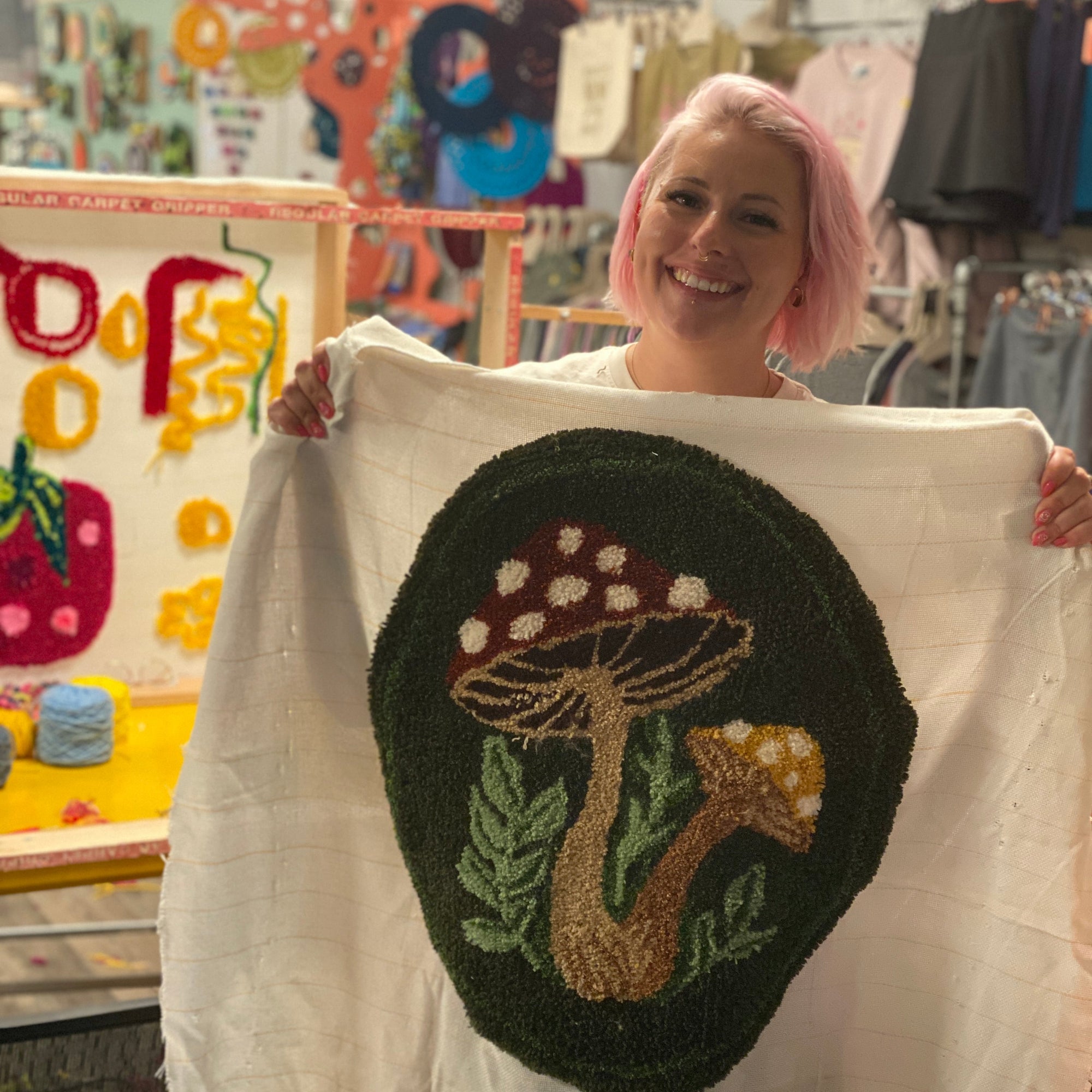 Person holding a tufted mushroom design on a white fabric in a craft store.