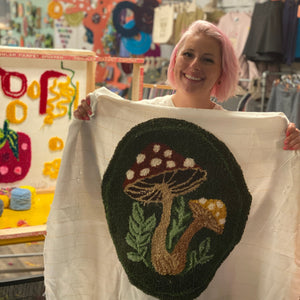 Person holding a tufted mushroom design on a white fabric in a craft store.