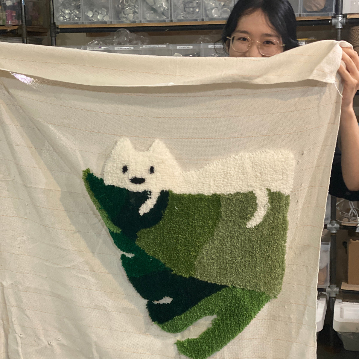 Person holding a tufted art piece with a cat design.