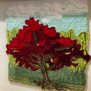 Tufted art piece with red and green patterns on a light background. 