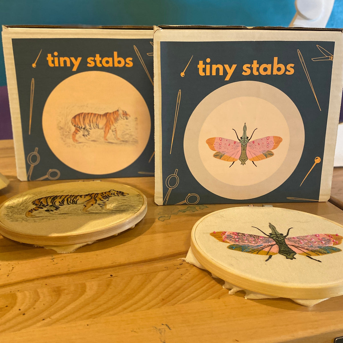 Two embroidery kits titled 'tiny stabs' with illustrations of a tiger and a moth, accompanied by completed, embroidered samples of the designs.