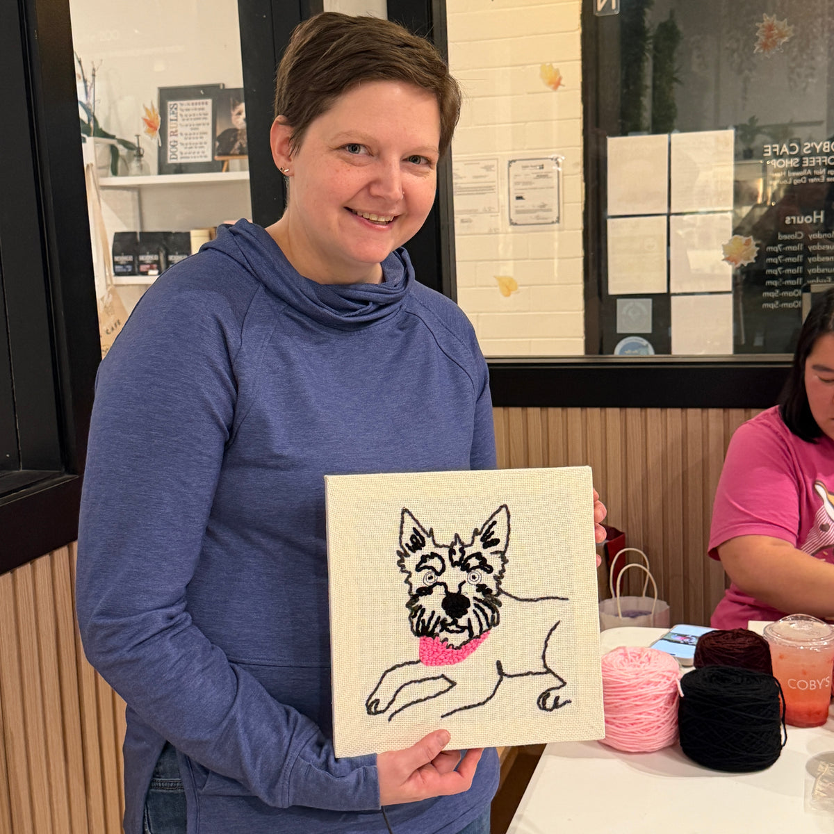 Person holding a punch needle portrait of a dog in a casual setting.