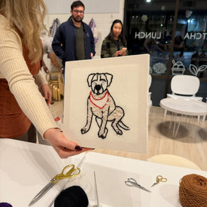 Person holding a punch needle portrait of a dog in a casual indoor setting. 