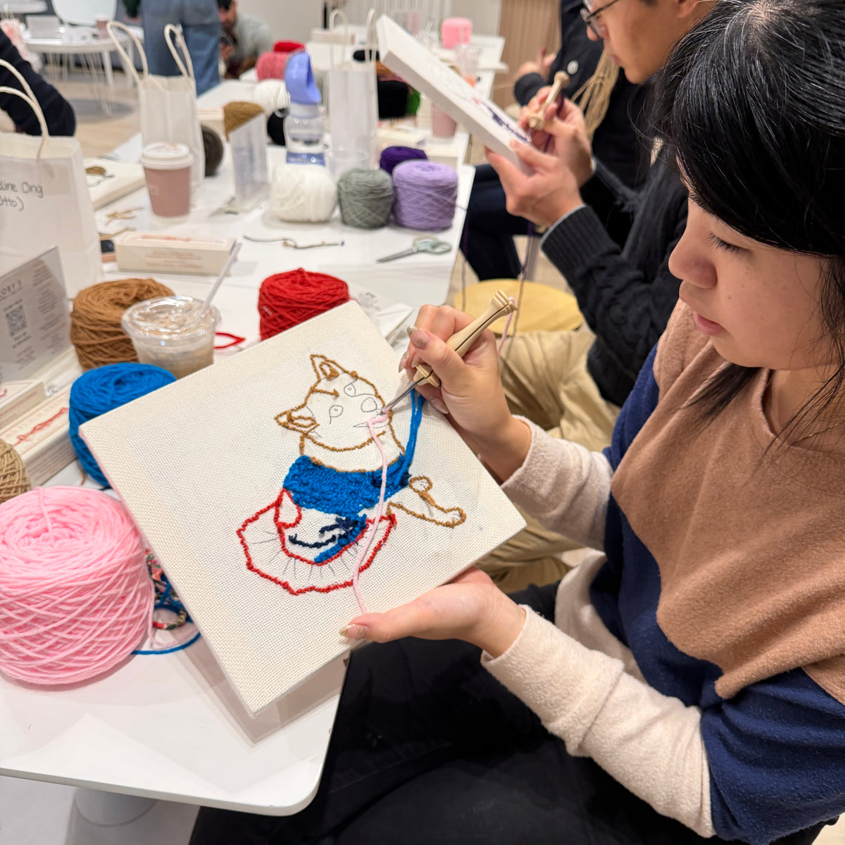 Person working on a punch needle pet portrait with yarn and tools at a craft workshop.