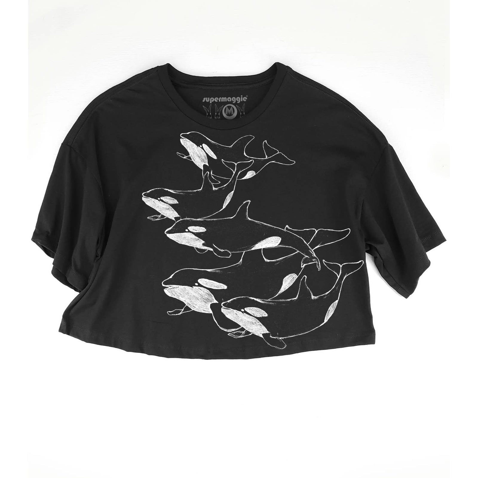 A black short-sleeve crop top t-shirt featuring a white line art graphic of five orcas swimming together across the front. The brand name 'supermaggie' is printed inside the collar.