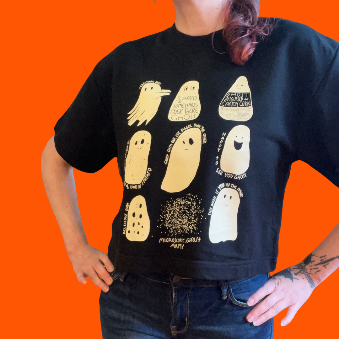 A person wearing a short sleeve, cropped black sweatshirt with illustrations of nine different ghosts screenprinted in cream colored ink. 
