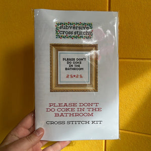 Cross stitch kit packaging with text and a small image of a framed cross stitch design that says, "Please don't do coke in the bathroom" and has bunnies and a border on a yellow background.