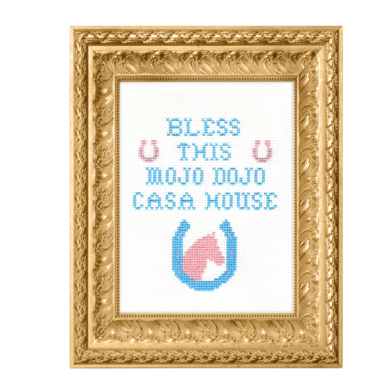 A finished cross stitch framed in an ornate gold frame. The cross stitch says "Bless this Mojo Dojo Casa House" and has a horse and horse shoe at the bottom. 