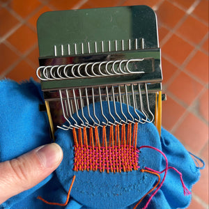 Handheld loom with woven fabric on a tiled floor background