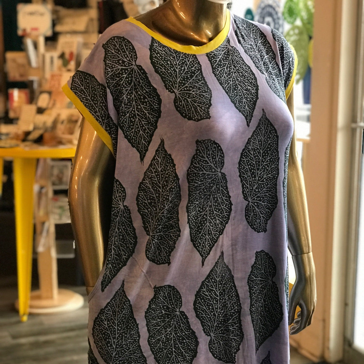 Mannequin wearing a dress with forest freen leaf pattern on a blurred indoor background. 