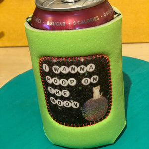Green can cooler with patch on the front that says "I Wanna poop on the moon" It is holding a maroon can of soda.