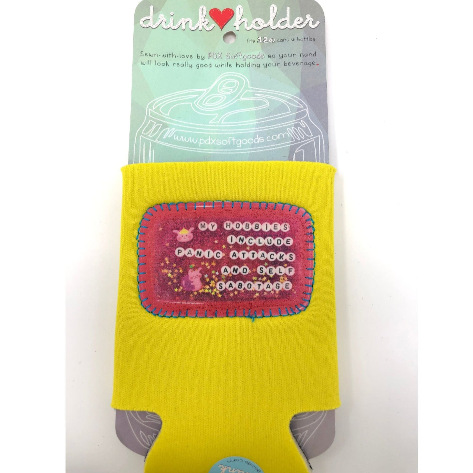 Yellow drink holder with pink patch on a white background. It says "My hobbies include panic attacks and self sabotage."
