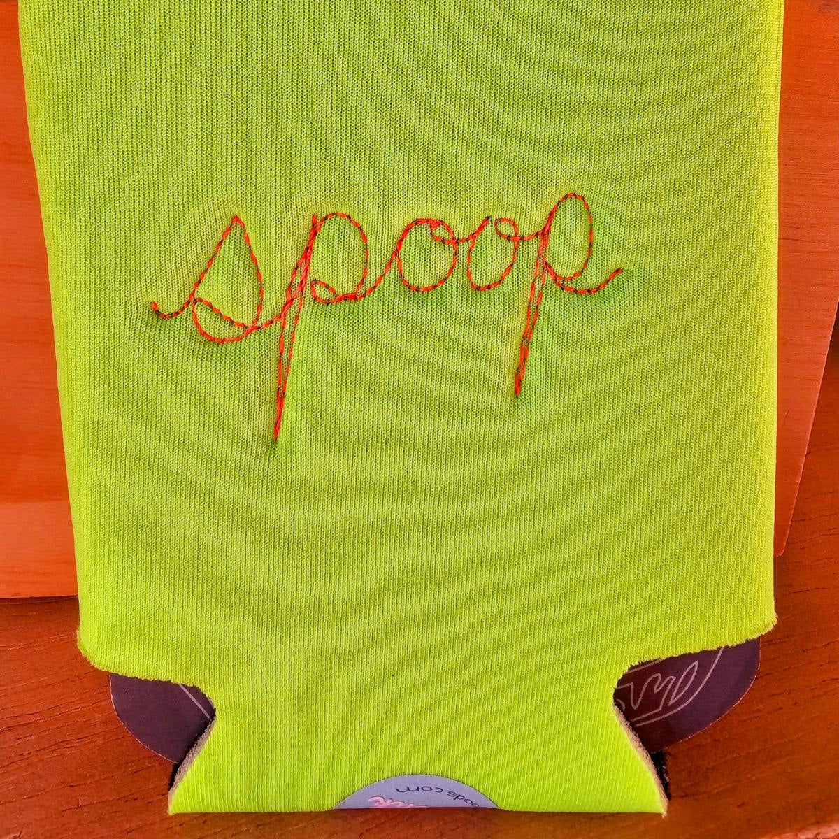 A bright lime green neoprene can cooler sleeve with the word 'spoop' embroidered in orange-  shown on a wooden surface.