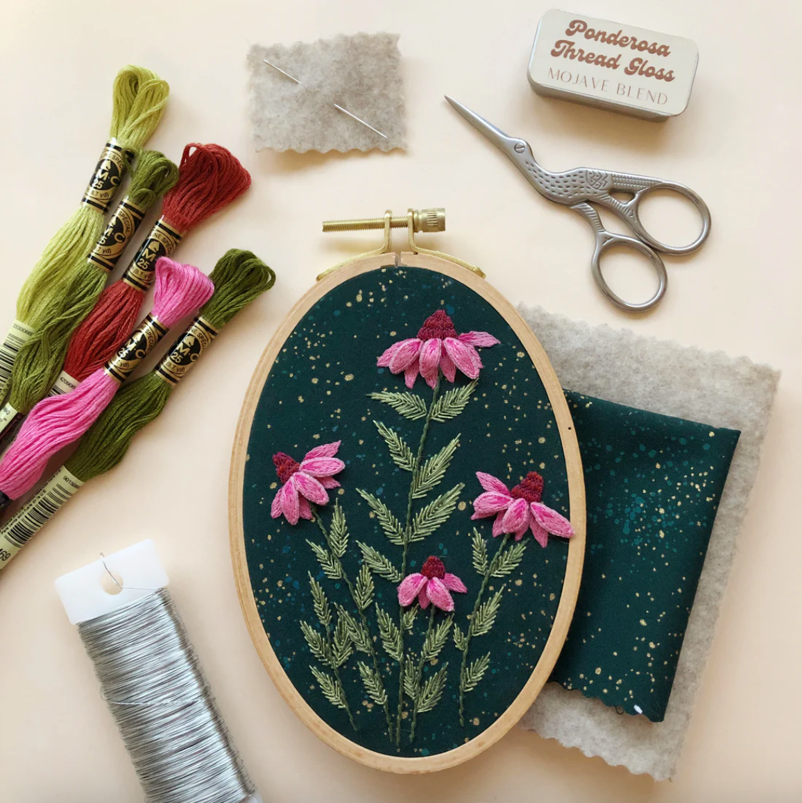 Embroidery hoop with floral design, threads, scissors, and thread gloss on a beige background. 