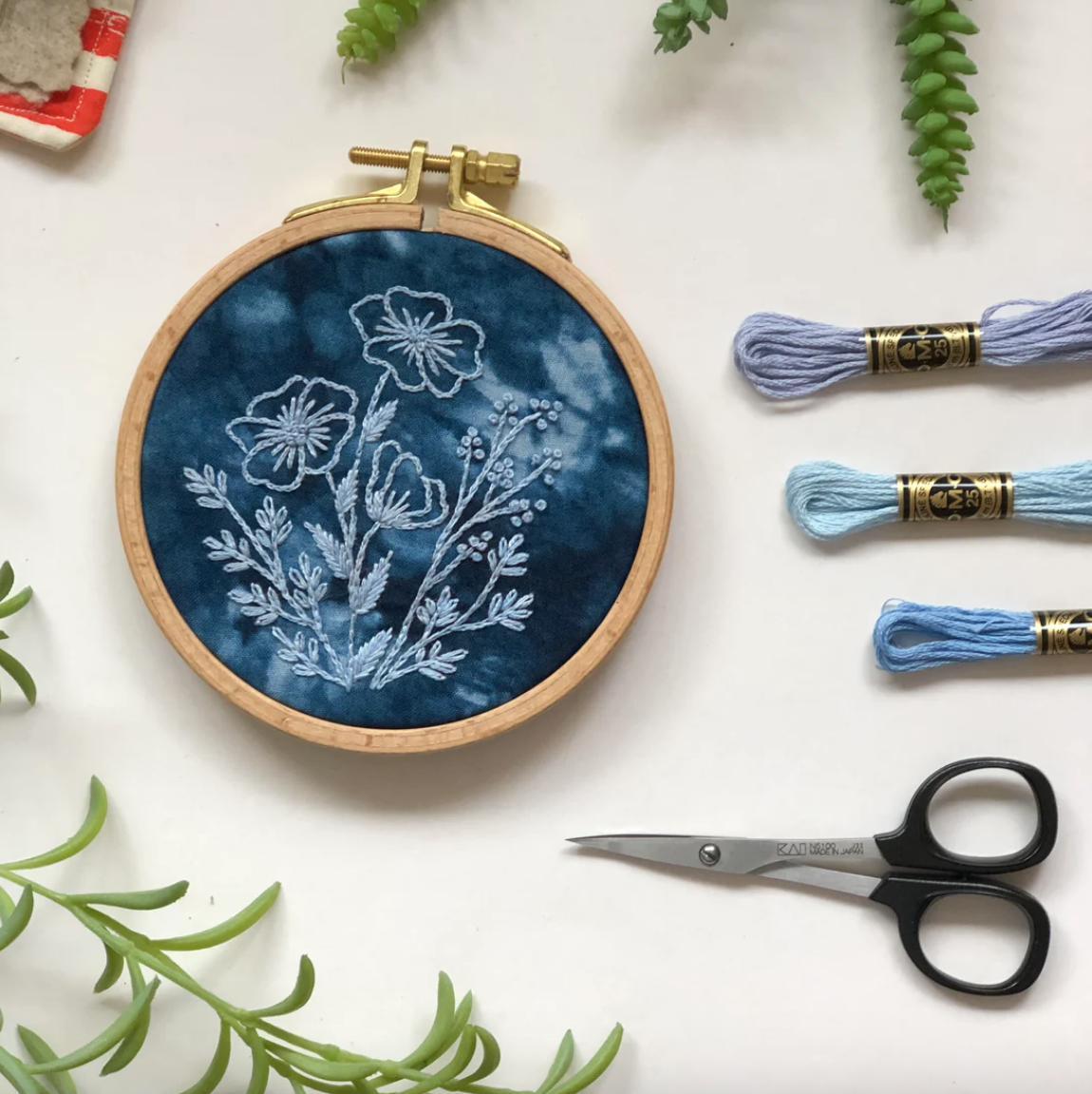 Embroidery hoop with floral design, embroidery threads, and scissors on a white background. 