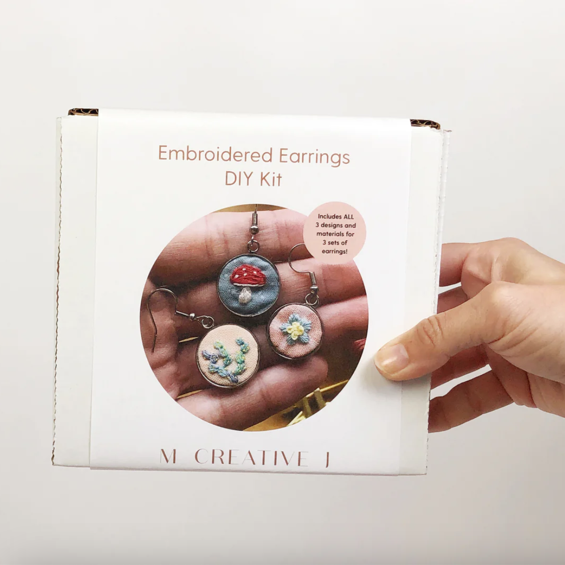 Embroidered Earrings DIY Kit packaging held by a hand on a light background. 
