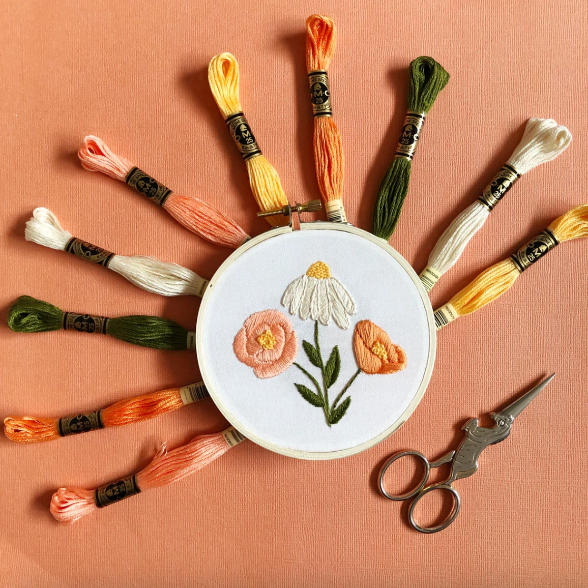 Embroidery hoop with floral design and embroidery threads on a peach background
