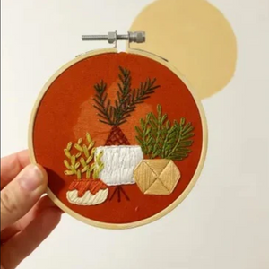Embroidery hoop with embroidered plants on a rust background.