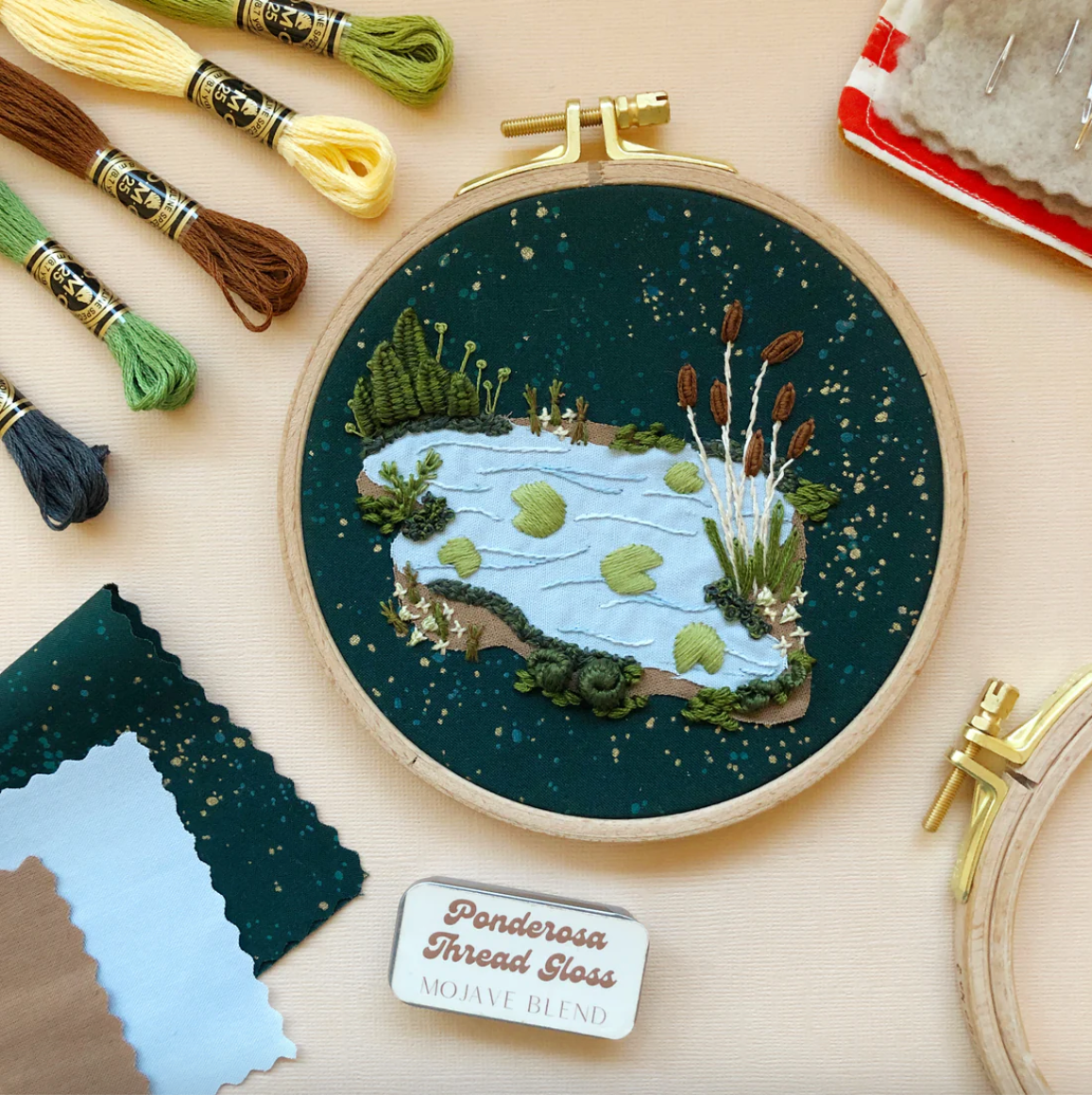 Embroidery hoop with nature-themed design on a table with embroidery threads and tools.