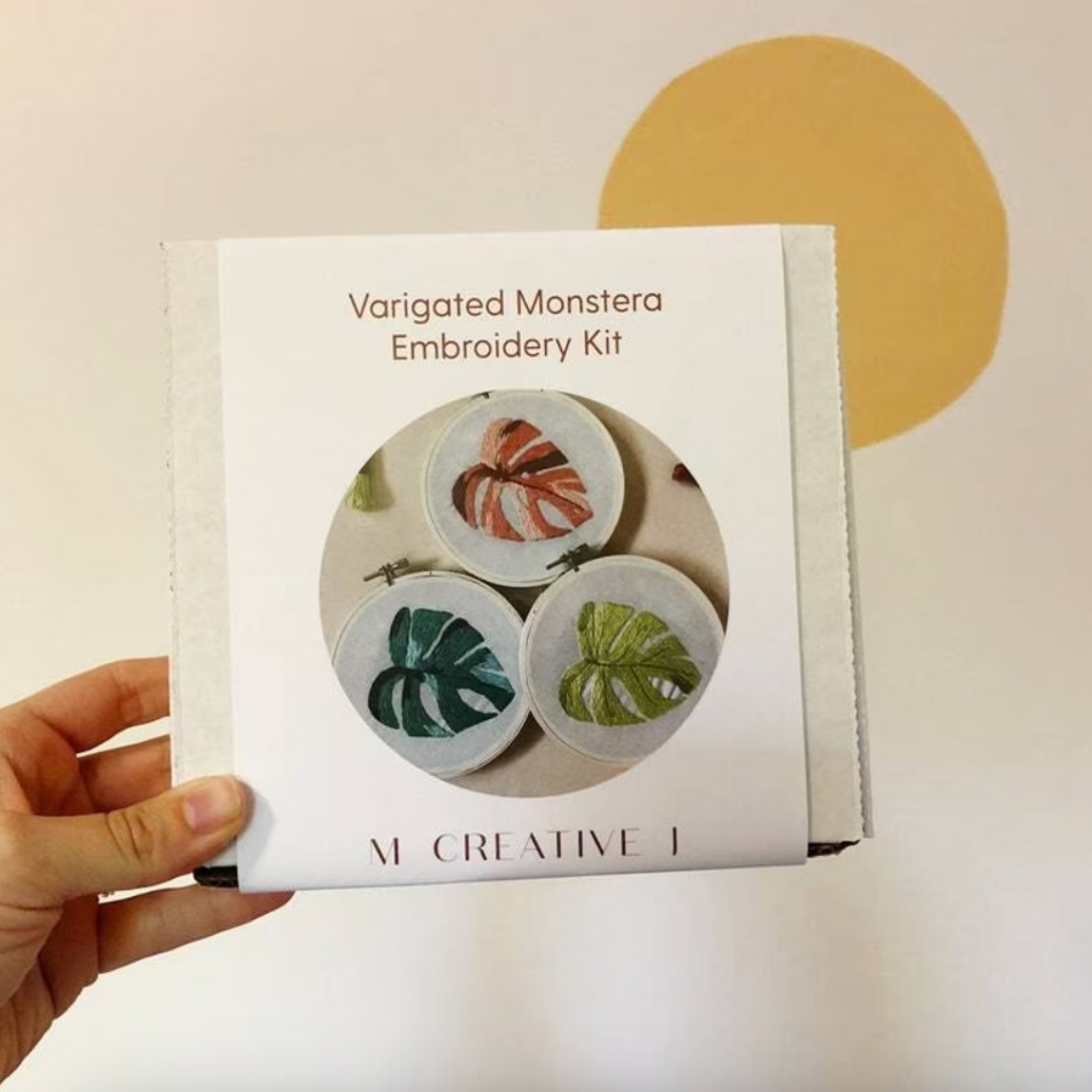 Variegated Monstera Embroidery Kit packaging held by a hand with a beige background