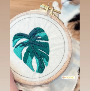 Embroidery hoop with green leaf design held by a person. 