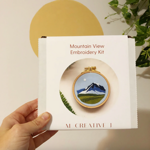 Mountain View Embroidery Kit packaging held by a hand with a plant in the background