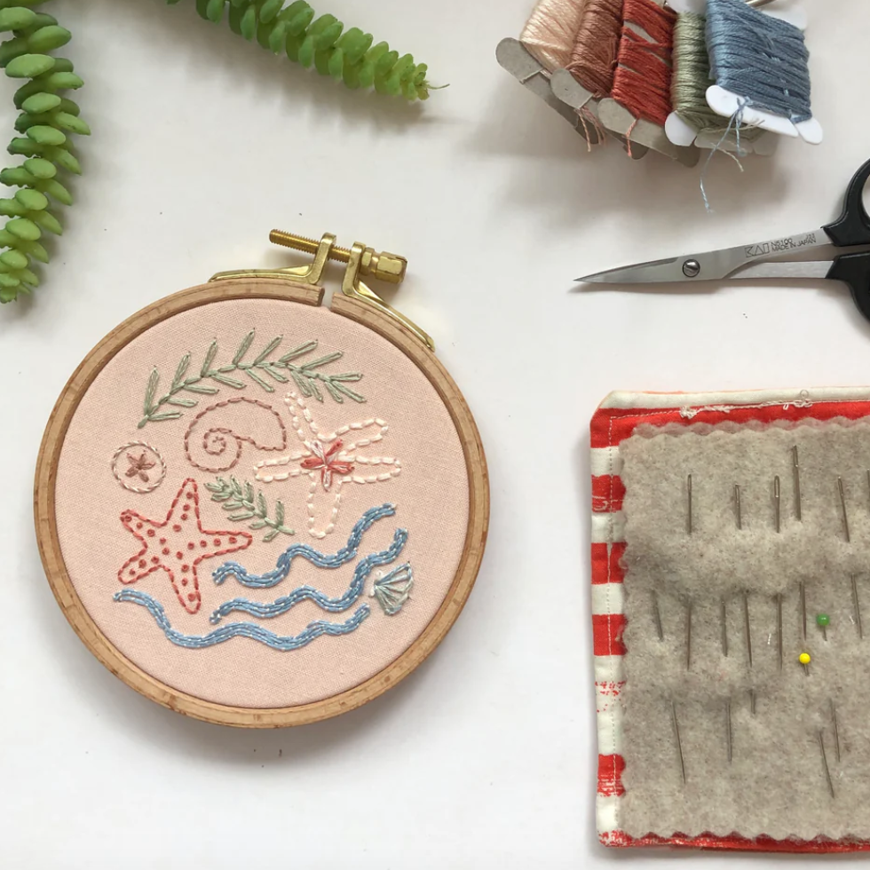 Embroidery hoop with starfish design, scissors, thread spools, and a fabric pad on a white surface.
